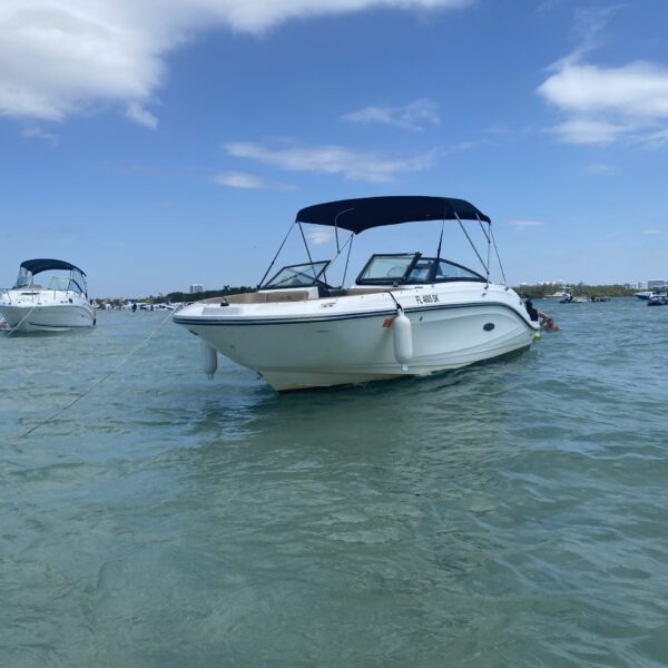 Side view of a 23′ Sea Ray SPX 230 bowrider with a black bimini top, anchored in shallow turquoise water in Miami under blue skies.